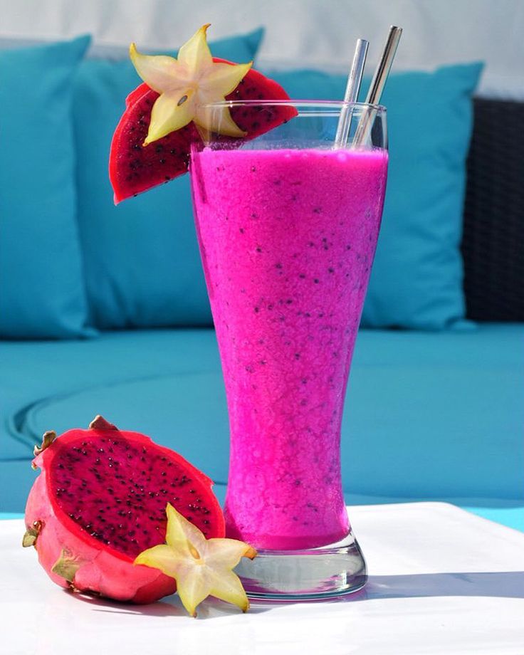 a pink smoothie in a tall glass next to a cut up dragon fruit