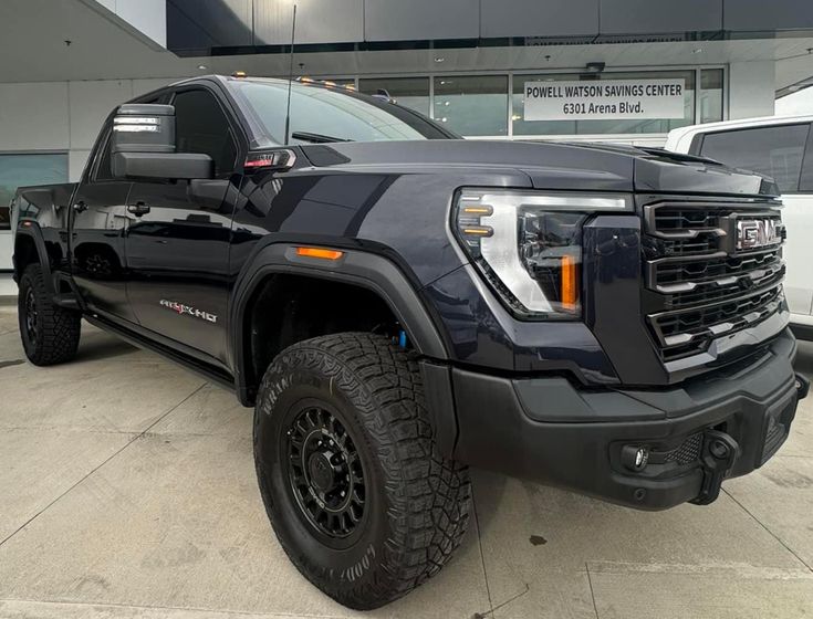 a black truck parked in front of a building with other trucks behind it on display