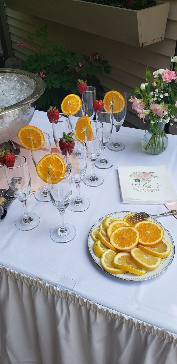 a table topped with lots of orange slices and wine glasses next to a bowl of strawberries