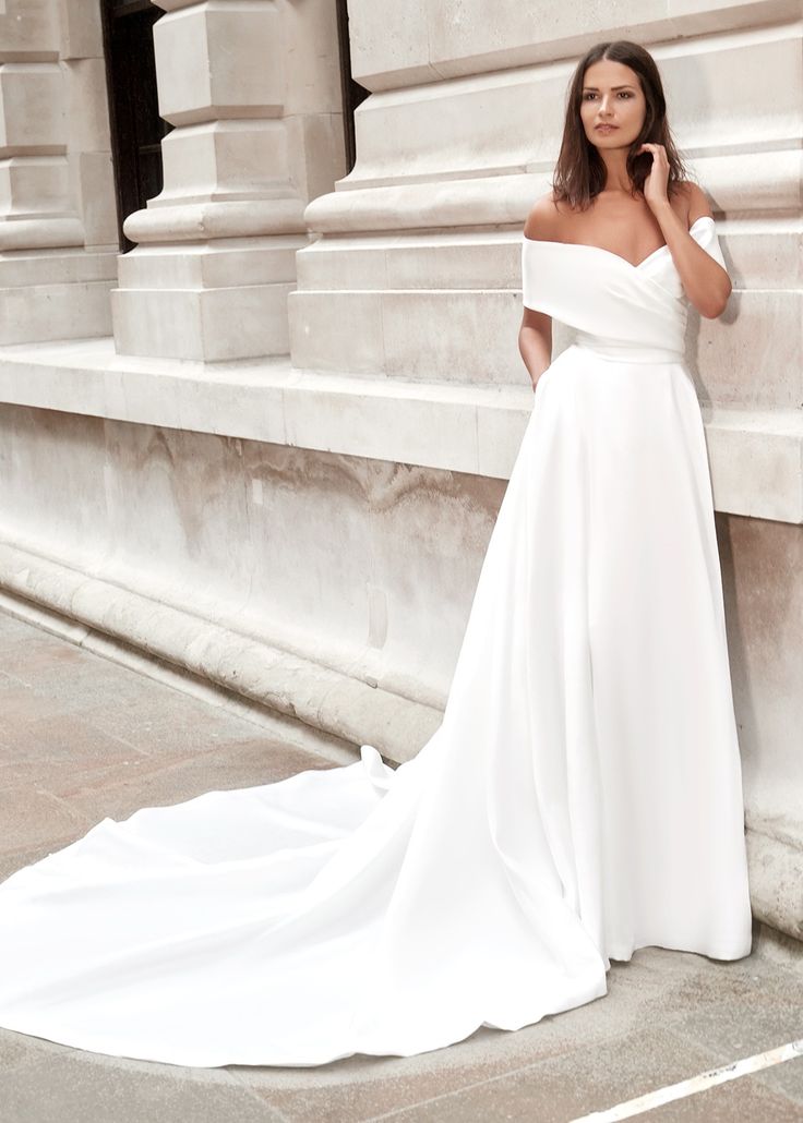 a woman in a white wedding dress leaning against a wall with her hand on her face