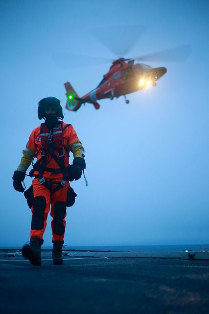 a man in an orange and black uniform standing next to a helicopter