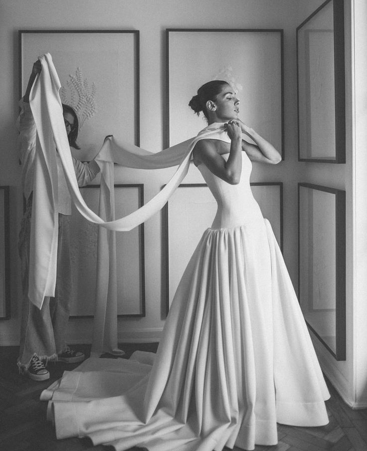 black and white photograph of woman in wedding dress with veil draped over her head, standing next to mannequins