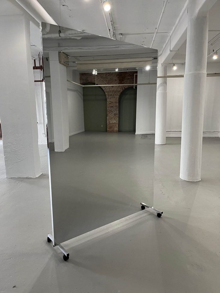 an empty room with white walls and flooring is shown in this image, there is a large mirror on the wall