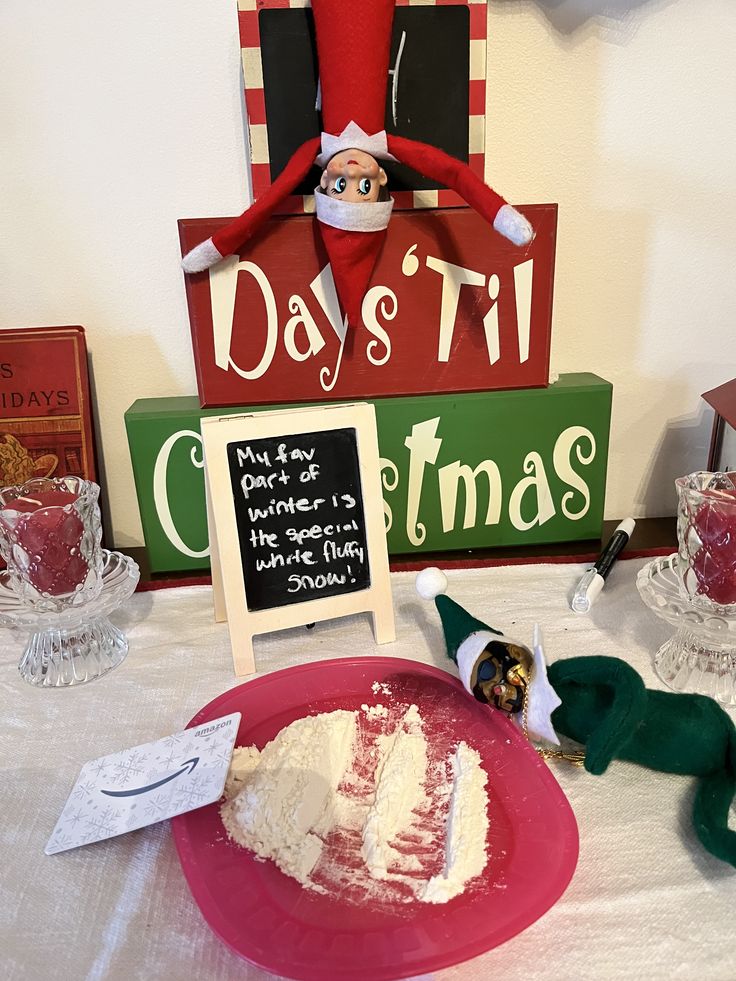 an elf is sitting on top of a sign next to a plate with cake and marshmallows