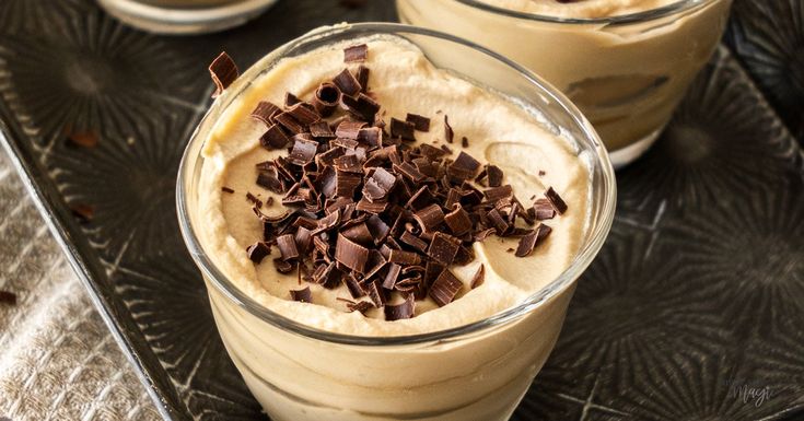 two glasses filled with dessert sitting on top of a metal tray covered in chocolate chips