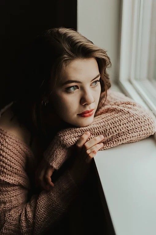 a woman leaning on a window sill with her arms crossed and looking out the window