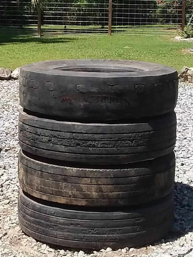 four old tires stacked on top of each other in the middle of a gravel area