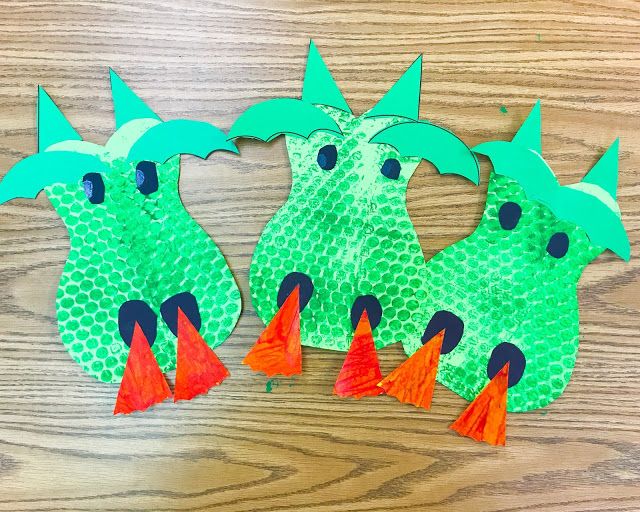 two green paper dragon puppets on a wooden table with orange tassels and one has an orange tail