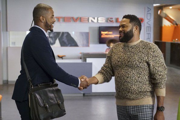 two men shaking hands in an office lobby, one is wearing a sweater and the other has a briefcase