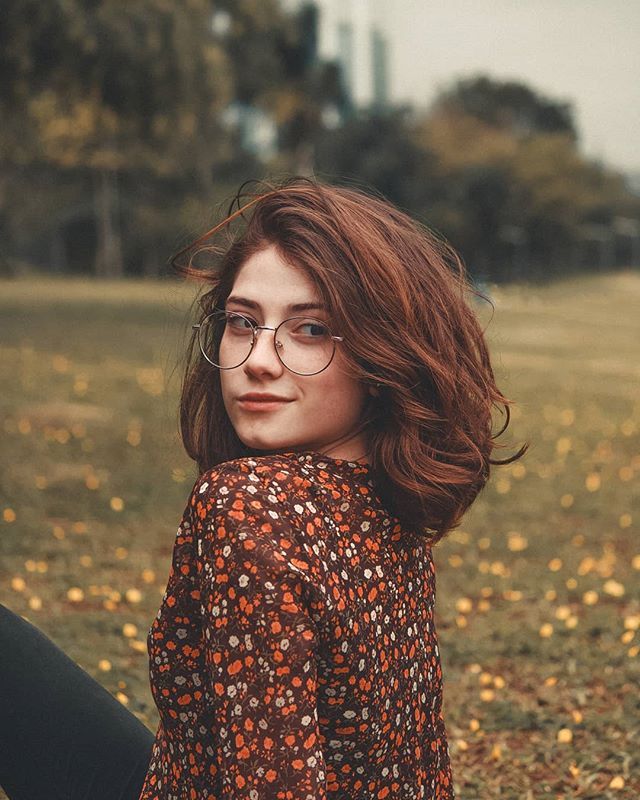 a woman wearing glasses sitting on the ground with her hair blowing in the wind and looking at the camera