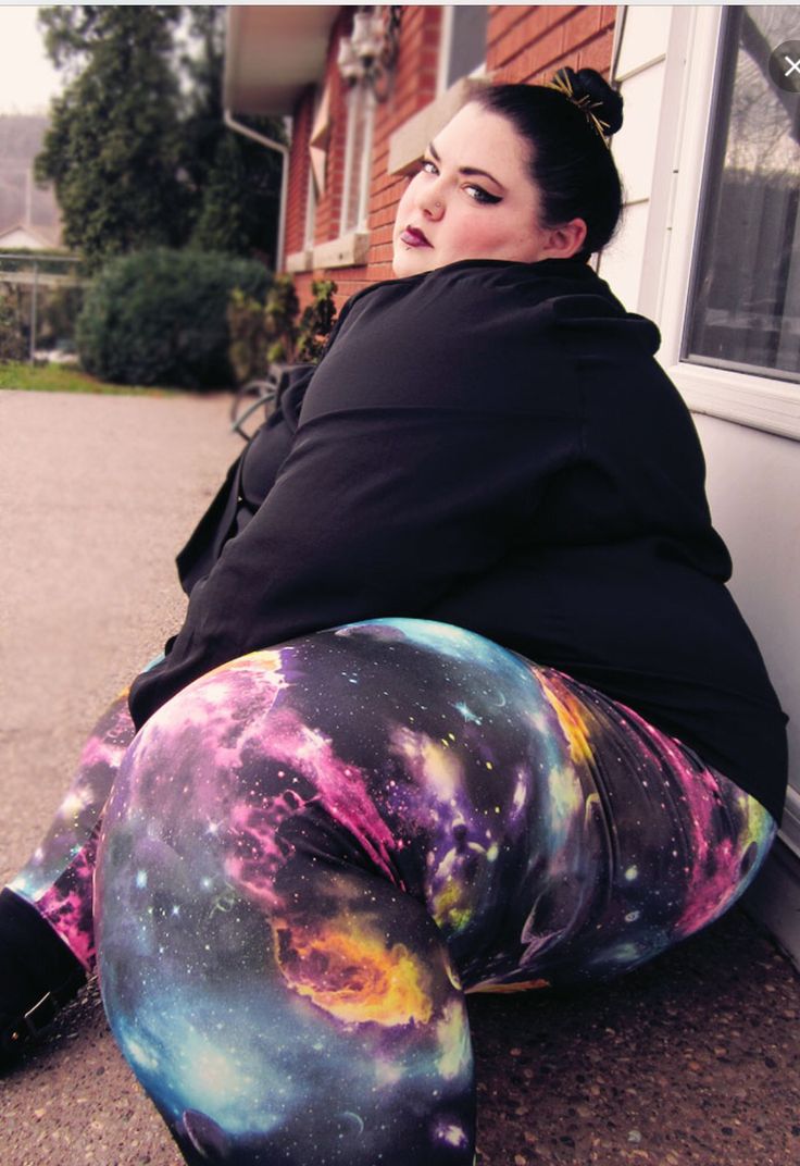 a woman is sitting on the ground wearing leggings with colorful galaxy print and black hoodie