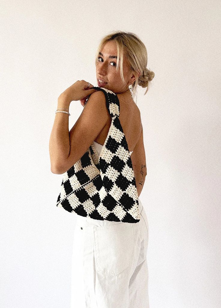 a woman in white pants and a black and white top is posing with her hand on her shoulder