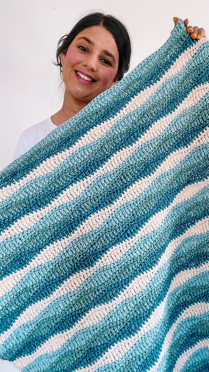 a woman is holding up a blue and white striped crocheted blanket that she made