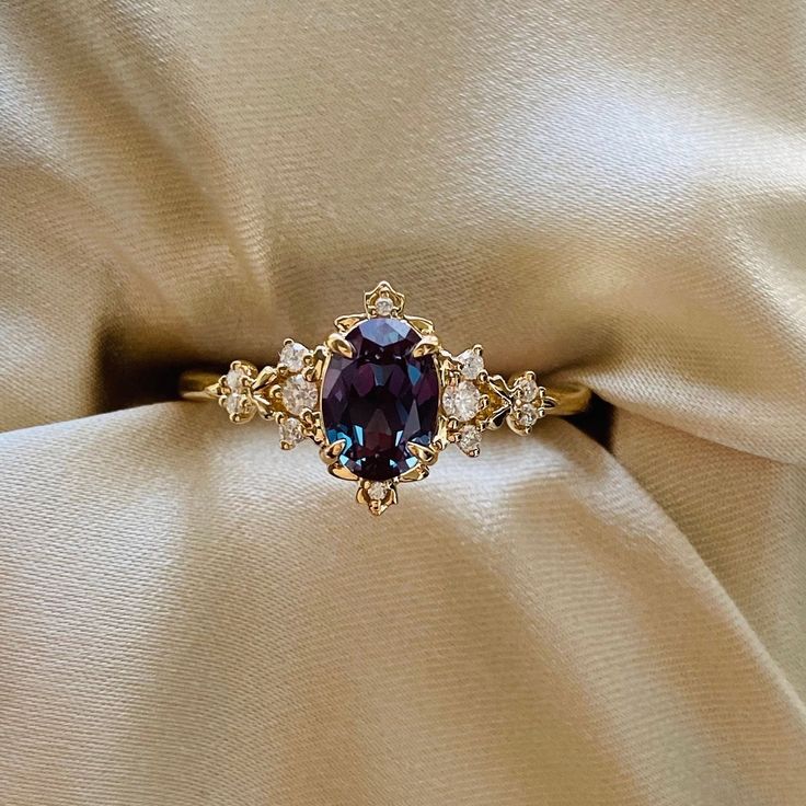 a ring with an oval shaped purple stone surrounded by smaller round diamonds on a beige satin background