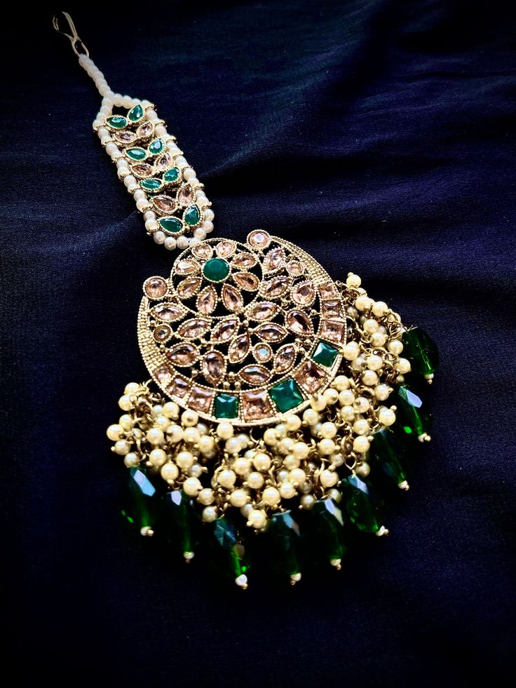 Alloy Based Necklace in gold color with forest green beads Enhanced with Stones, Beads and Artificial Pearls Adjustable cord to allow all size comfortable fit Set comes with with a matching pair of Earrings with chain , a Maang tikka and a passa Earrings have a push pin closure To view this set on head to our Instagram page @jyotikapateldesigns. You can also book a video call appointment with at +1 945-444-2194 Green Stone Work Temple Jewelry Danglers, Traditional Green Danglers With Beads, Green Kundan Beaded Earrings, Traditional Green Beaded Jewelry, Green Temple Jewelry Danglers, Green Kundan Danglers With Fusion Style, Green Kundan Danglers In Fusion Style, Green Kundan Fusion Danglers, Green Necklaces With Latkans For Party