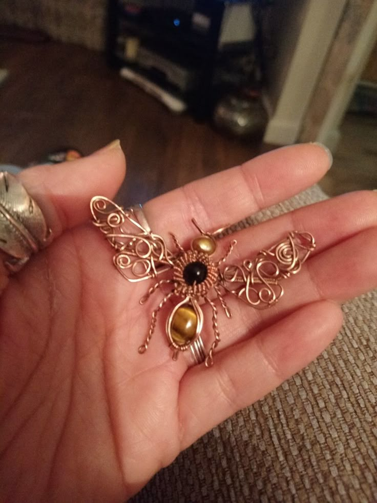 a person is holding some kind of insect brooch in their hand and it looks like they are made out of wire