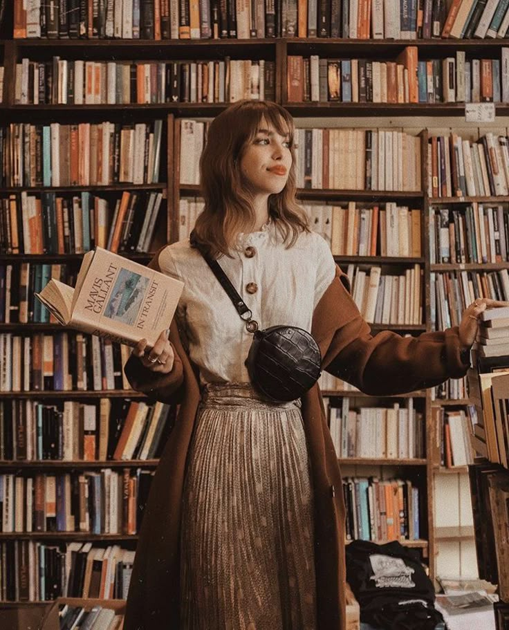 a woman standing in front of a bookshelf holding an open book and looking up