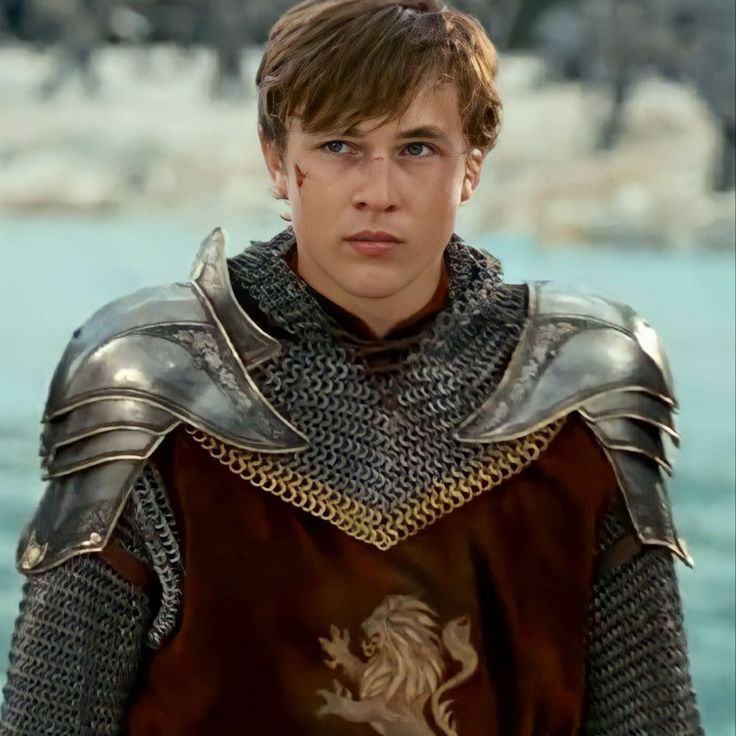 a young man dressed in armor standing by the water