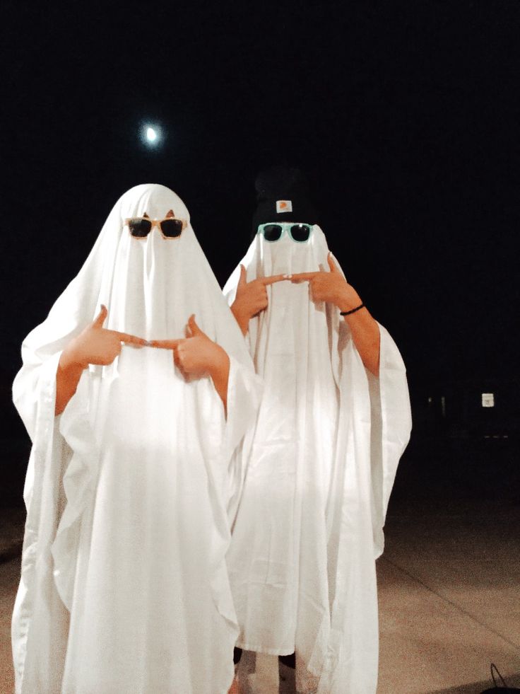 two people dressed in white standing next to each other with sunglasses on their heads and arms