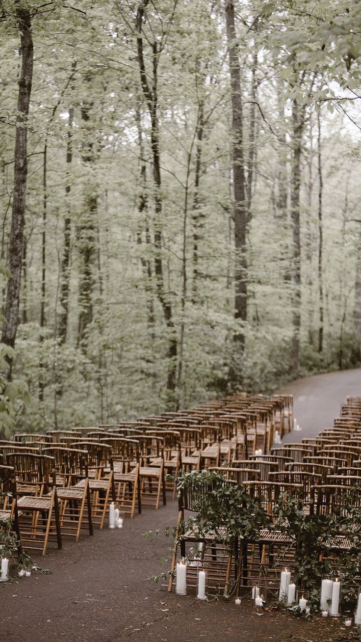 rows of wooden chairs set up in the woods for an outdoor ceremony with candles on them