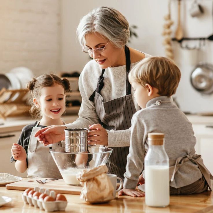 an older woman and two young children in the kitchen preparing food together with mixers