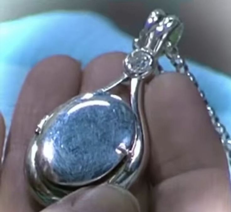 a close up of a person's hand holding a silver locke with a diamond on it