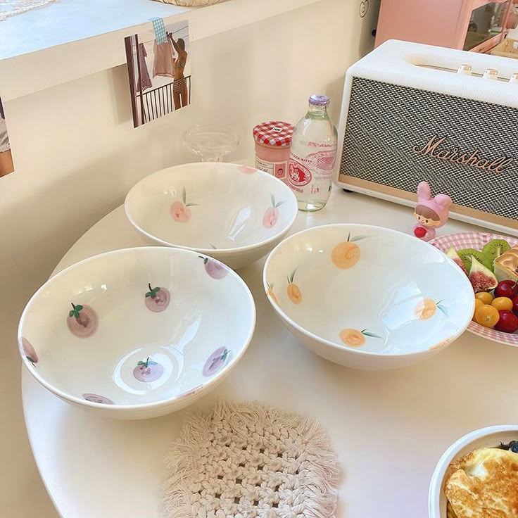 three white bowls with fruit on them sitting on a table next to a toaster