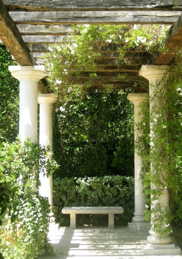 an empty bench in the middle of a garden with trees and bushes around it,