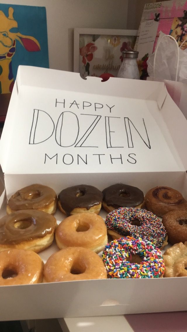 a box filled with lots of doughnuts on top of a counter next to a sign that says happy dozen months