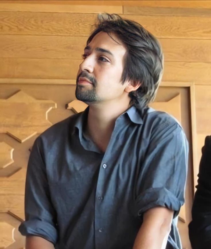 a man sitting in front of a wooden wall with his hands on his hips and looking off to the side