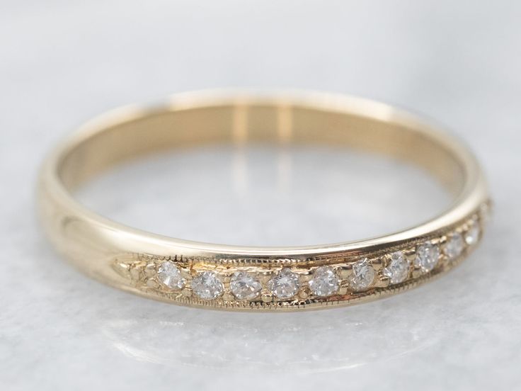 a gold wedding ring with five diamonds on it's side, sitting on a white surface