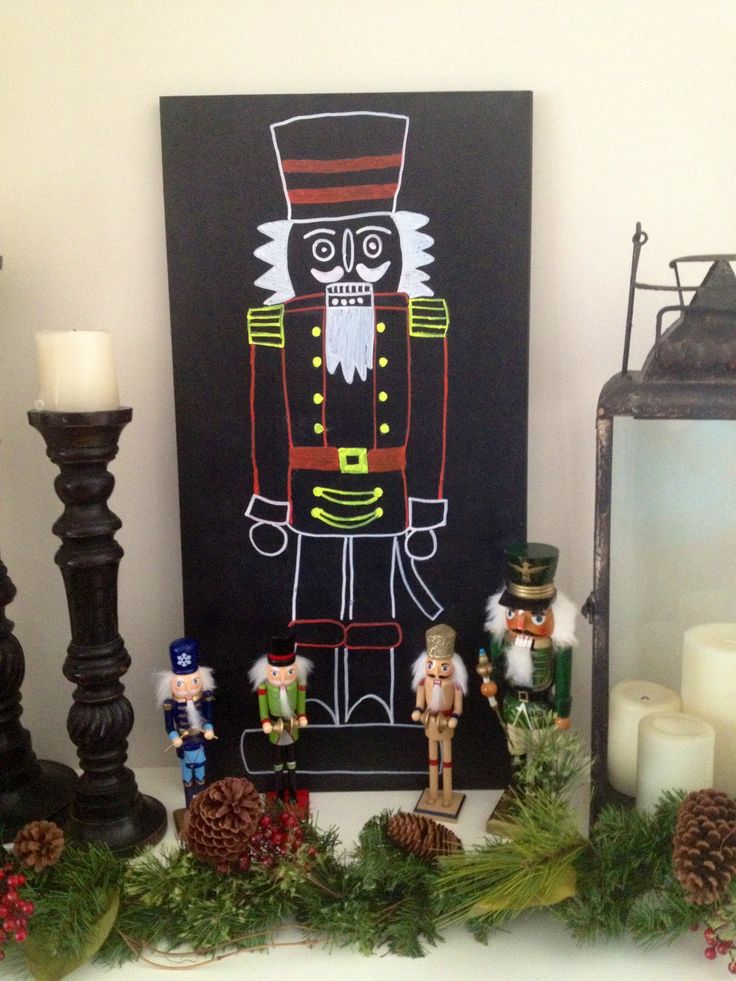 a christmas mantle with candles, decorations and a nutcracker painting on it's black board