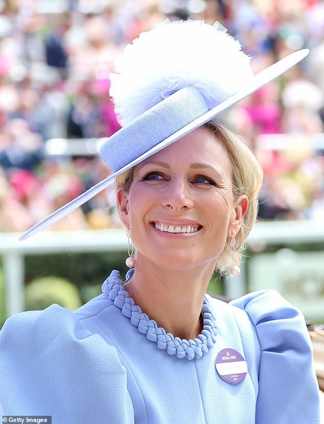 a woman wearing a blue hat with a white feather on it at a horse race