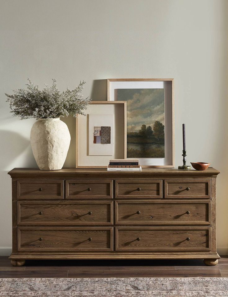 there is a vase with some flowers on top of it next to a dresser and pictures