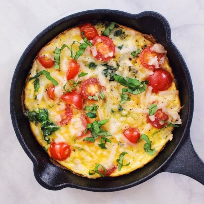 an omelet with tomatoes and spinach in a cast iron skillet on a marble surface