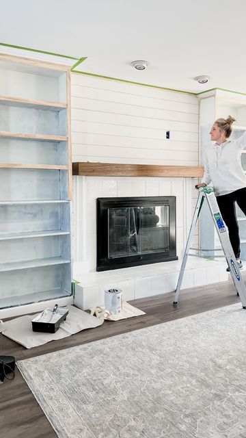 a woman standing on a ladder in front of a fire place and painting the walls