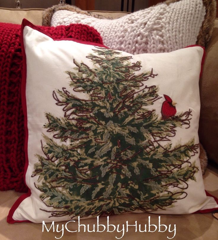 a christmas tree pillow on a couch with red trimmings and a cardinal sitting on it