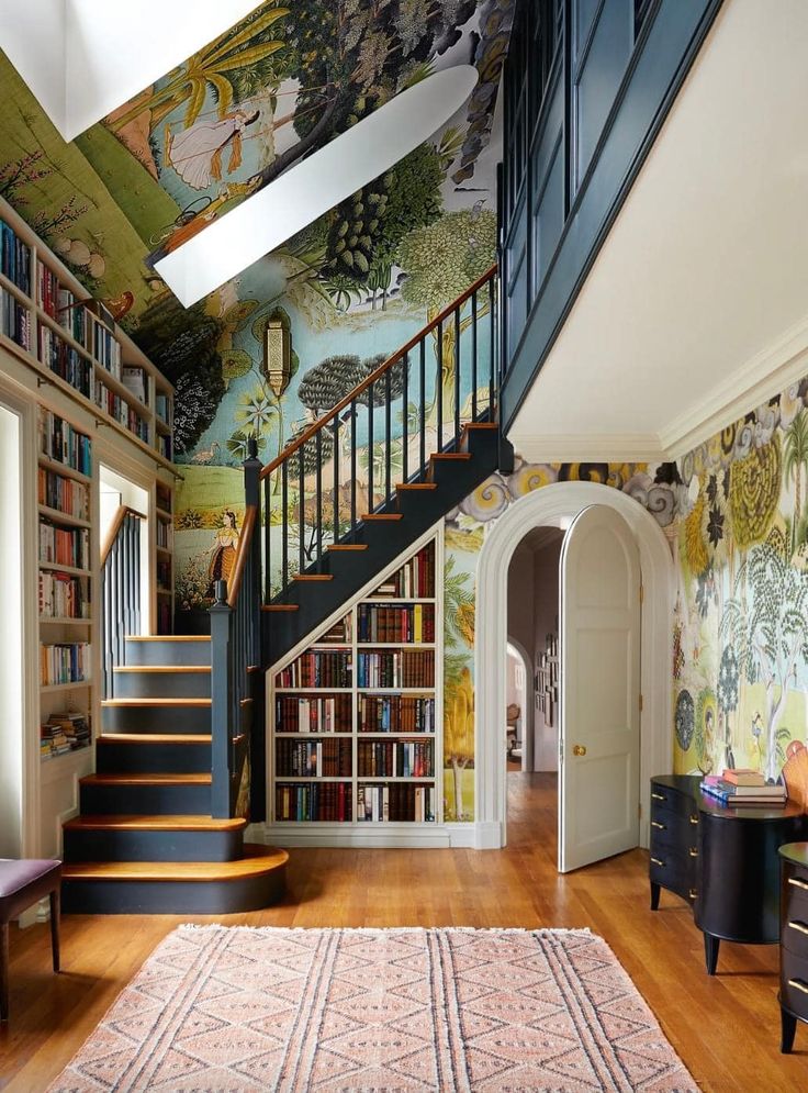 a room with stairs, bookshelves and paintings on the walls