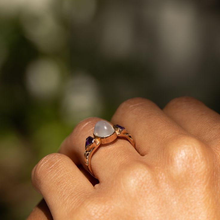 The Story A beautiful and luminous vintage ring done in 14 karat rose gold. At the center sits an oval shaped moonstone cabochon within a bezel setting. On either side is a triangular cuts amethyst adding a great pop of color. The center sits on a simple band. It measures 0.42 inches at center and looks great on the finger. Moonstones, which legend says bring the wearer good luck, are seen with adularescence, which this beautifully piece shows. The Specs Style Number: R2474 Vintage, circa 20th C 14k Gold Cabochon Moonstone Promise Ring, Heirloom Moonstone Promise Ring, Heirloom Oval Cabochon Moonstone Ring, Rose Gold Moonstone Ring With Rose Cut Diamonds, Rose Gold Oval Cabochon Gemstone Ring, Heirloom Rose Gold Birthstone Ring With Gemstone, Heirloom Rose Gold Cabochon Rings, Heirloom Rose Gold Birthstone Ring, Fine Jewelry Rose Gold Moonstone Ring