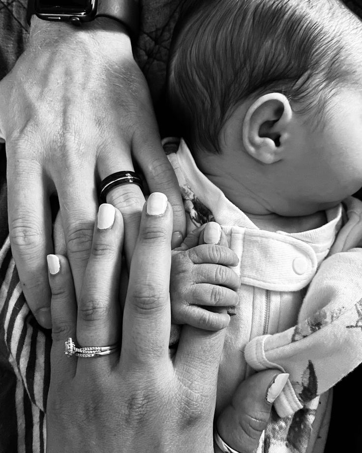 a black and white photo of a baby being held by two adults with their hands