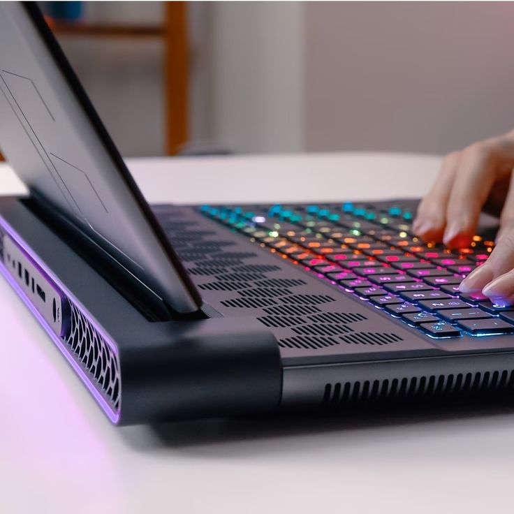 a close up of a person typing on a laptop computer with colorful lights coming from the keyboard