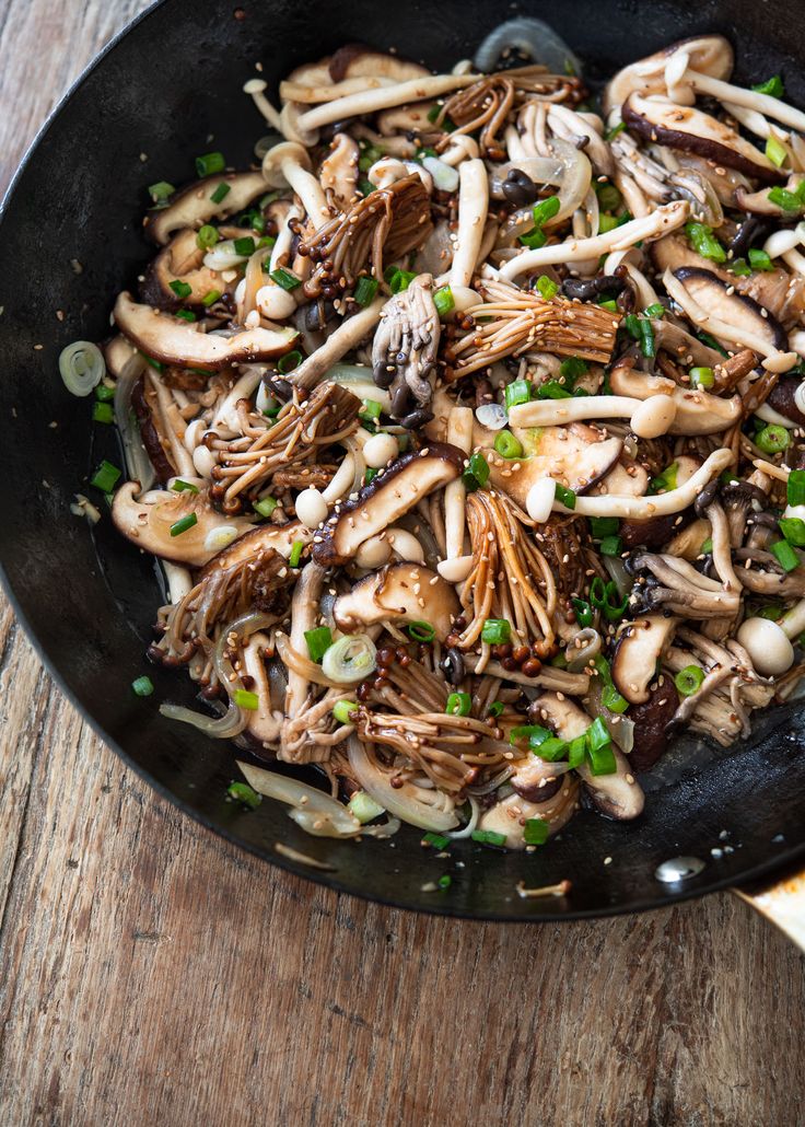 a skillet filled with mushrooms and onions on top of a wooden table next to slices of bread