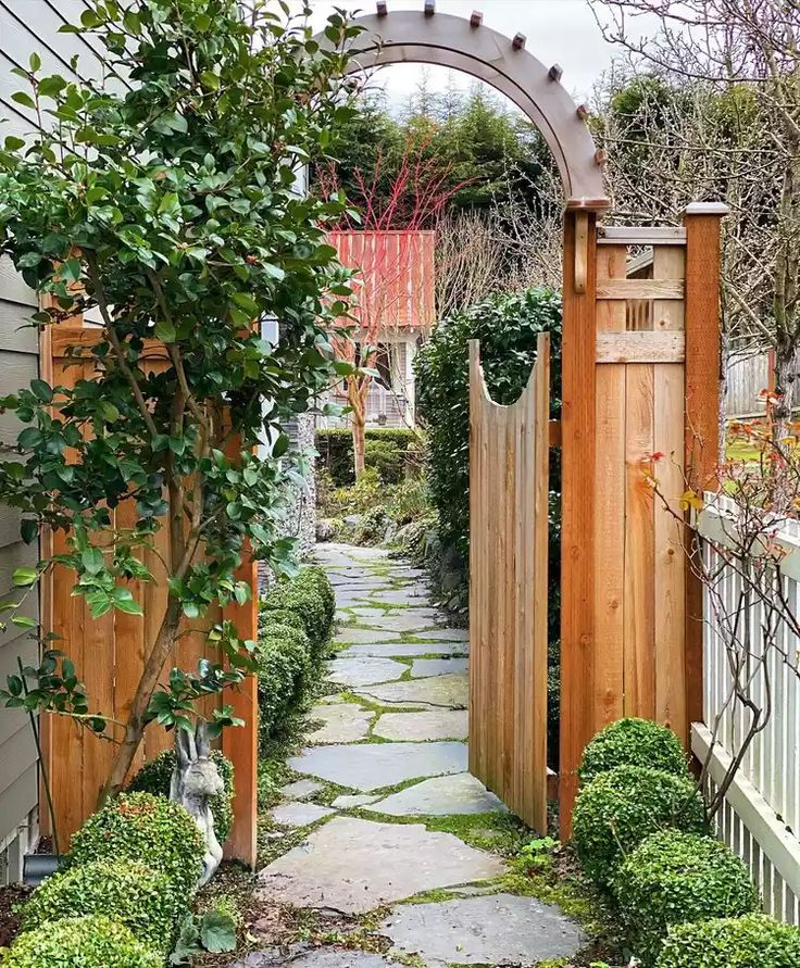 a stone path between two wooden gates leading into a yard with trees and bushes on either side