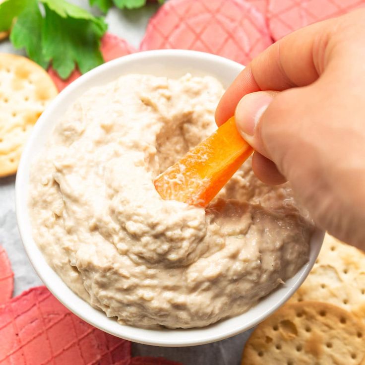 a hand dipping a carrot into a bowl of dip