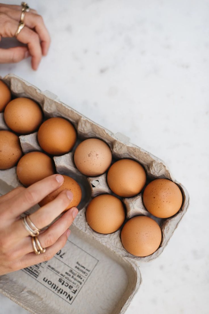 a woman is holding an egg in a carton on the table next to some eggs