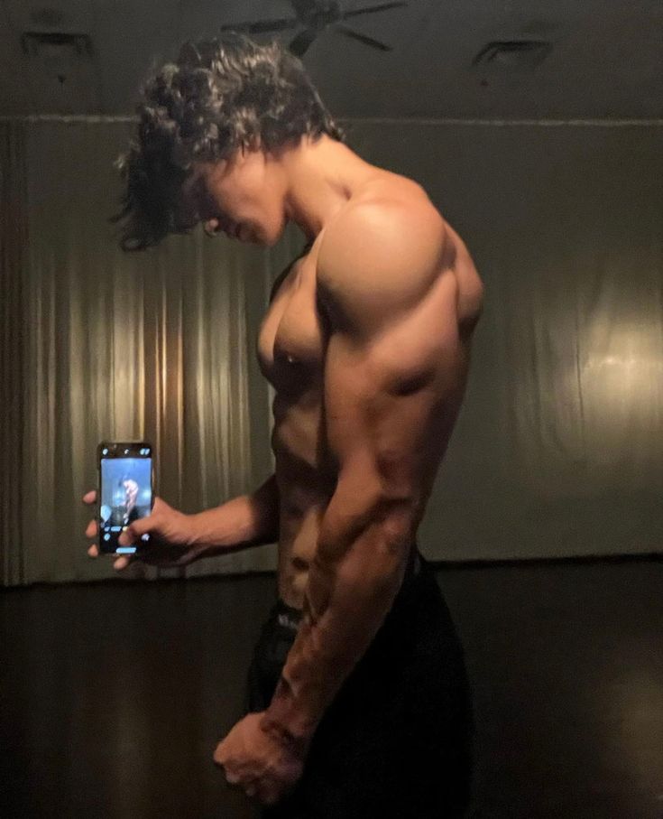 a shirtless man taking a selfie in front of a mirror with his cell phone