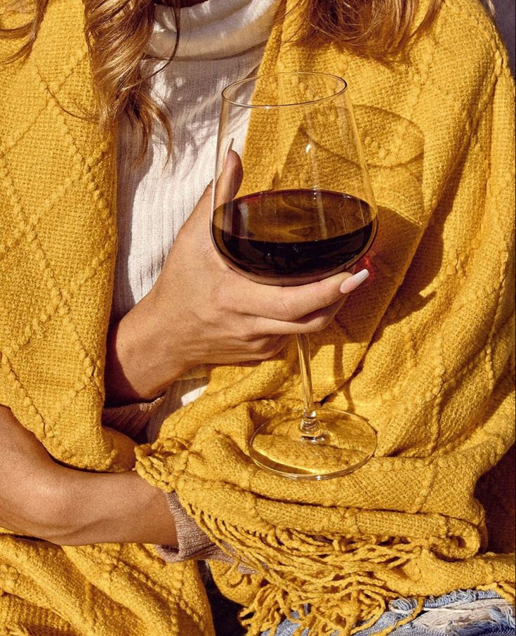 a woman holding a glass of wine in her hand and wearing a yellow shawl