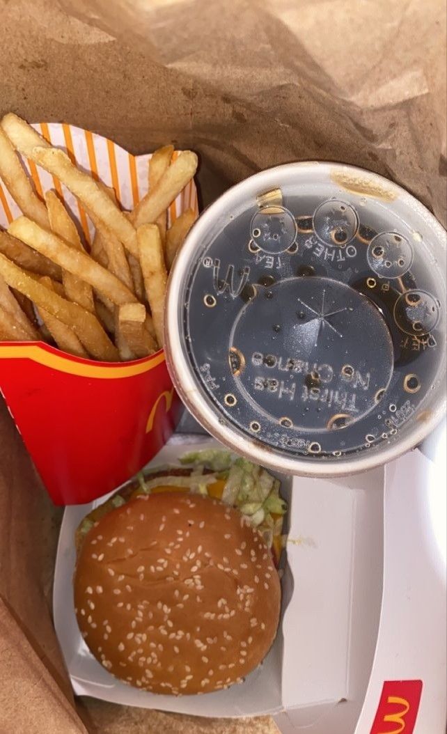 a hamburger and french fries in a paper container on a plate with a measuring cup