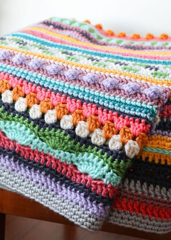 a multicolored crocheted blanket sitting on top of a wooden chair next to a window