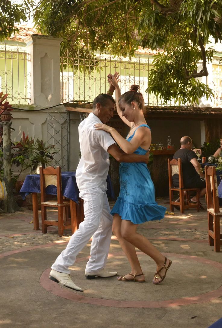 two people are dancing in the middle of an outdoor area with tables and chairs around them